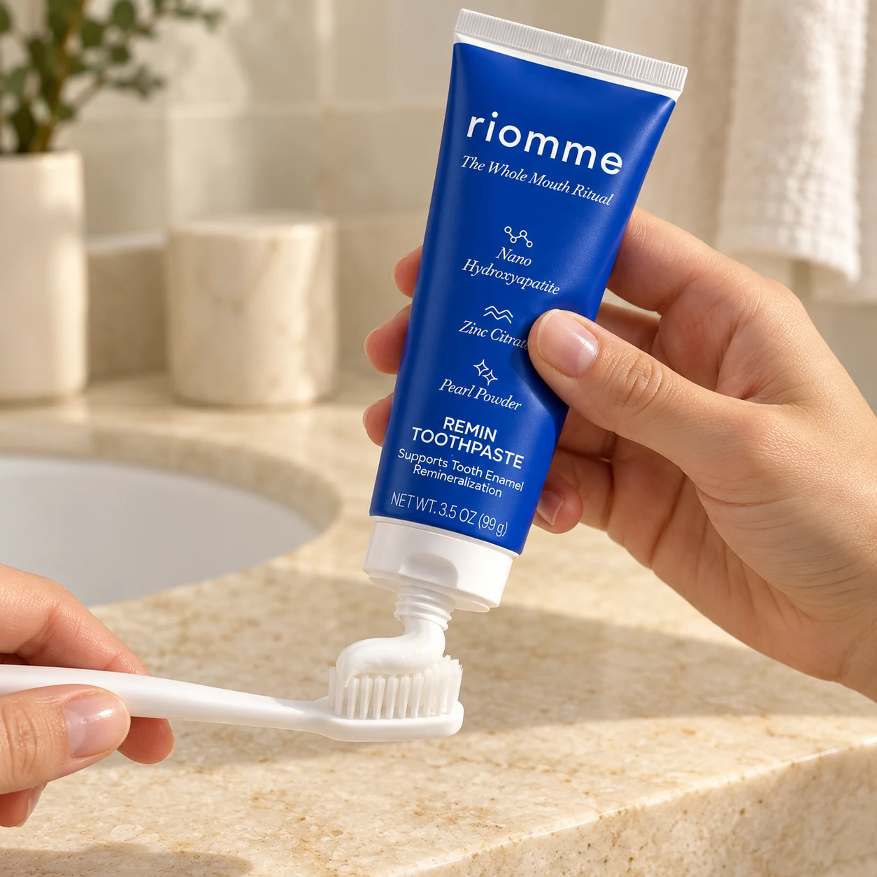 A hand squeezing Remin Toothpaste onto a toothbrush at a bathroom sink
